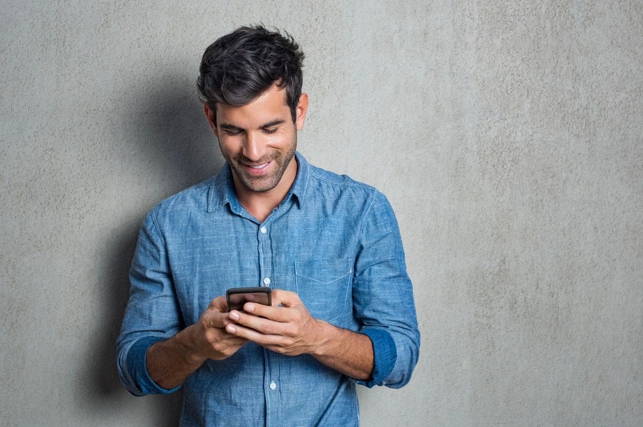 A man smiling while looking at his phone.