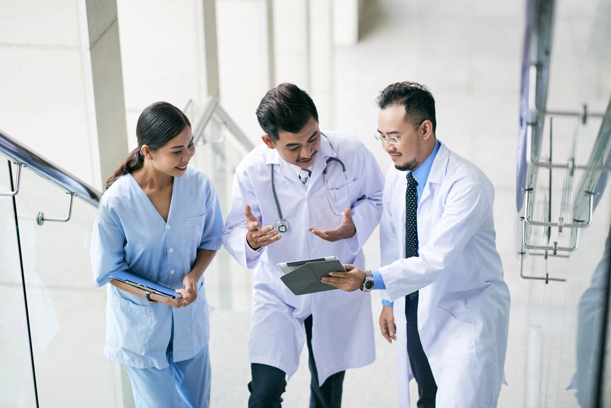 Three doctors are standing in a line and one is holding a tablet.