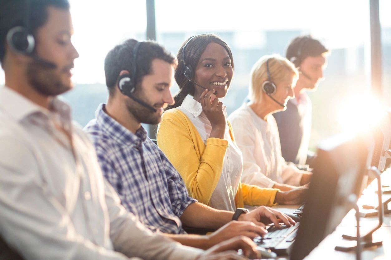 A group of people sitting at computers with headsets on.