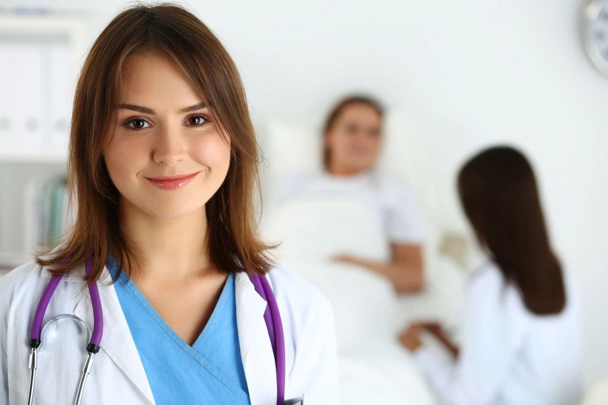 A woman in white lab coat standing next to two other women.